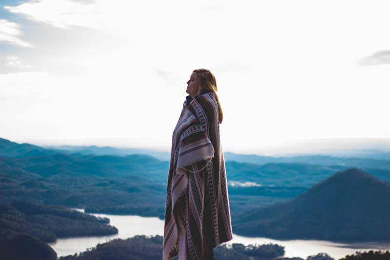 woman standing with blanket wrapped around her and mountains and water in the background