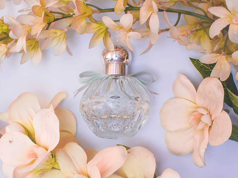 lay flat perfume bottle surrounded by peach colored flowers