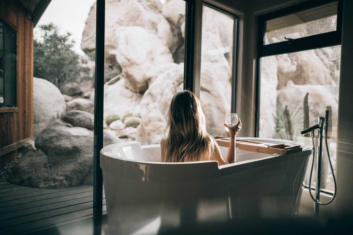 woman relaxing in a bathtub looking out windows on rock formations and holding a glass