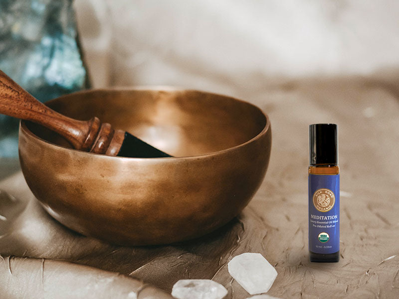 singing bowl and crystals next to a roller bottle of silk road organic's meditation essential oil blend