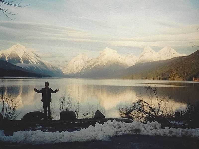 person standing in front of lake with snowcapped peaks in background