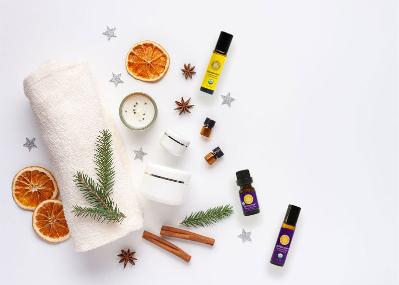 top down image of essential oil bottles, orange slices, cinnamon sticks, fir needles, anise and confetti stars with a rolled up towel and beauty containers