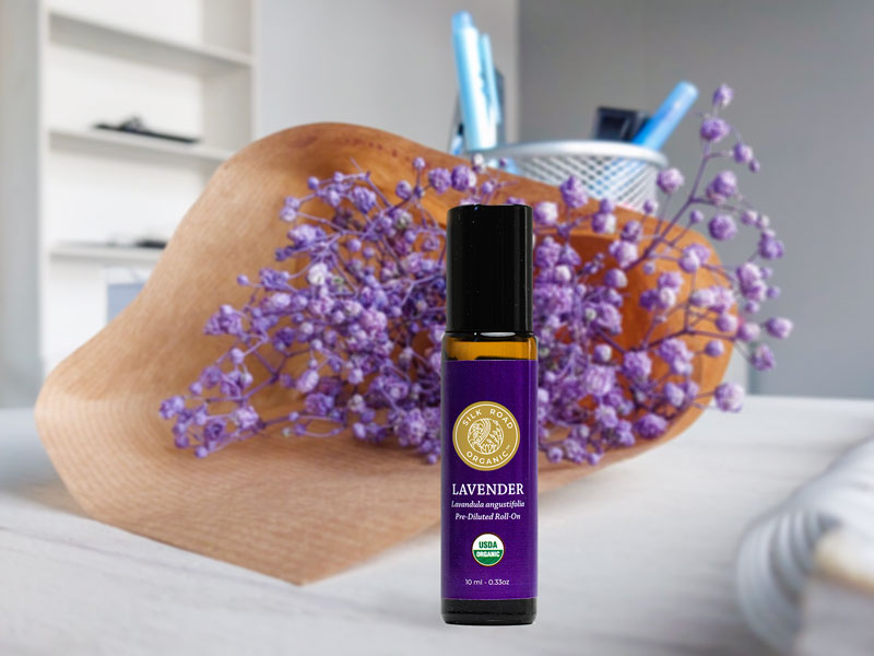 lavender essential oil roll-on sitting on a desk in front of purple flowers