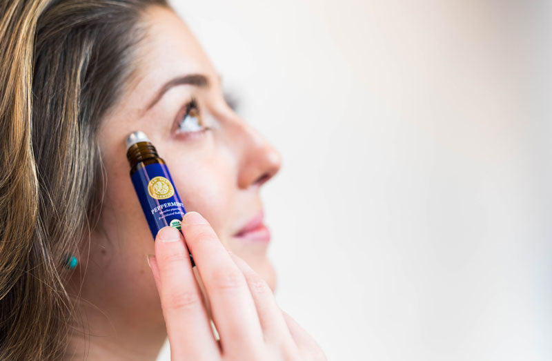 woman holding peppermint essential oil roll-on to temple