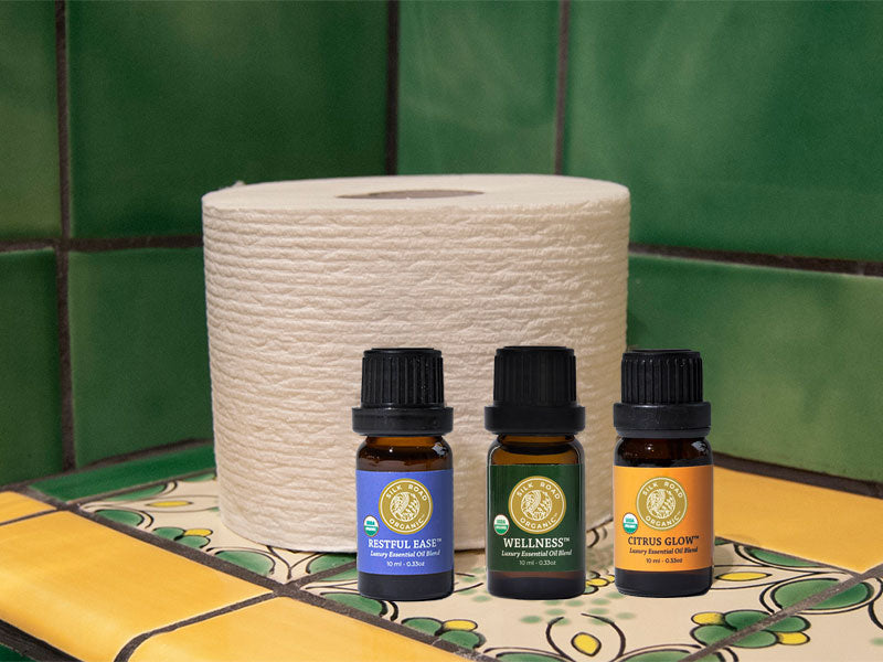 roll of toilet paper on a tile shelf with essential oil bottles lined up in front: restful ease, wellness and citrus glow blends