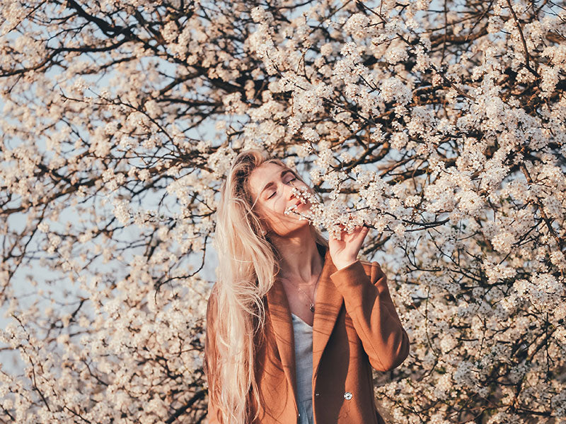 woman standing in front of a blooming tree, smelling the flowers