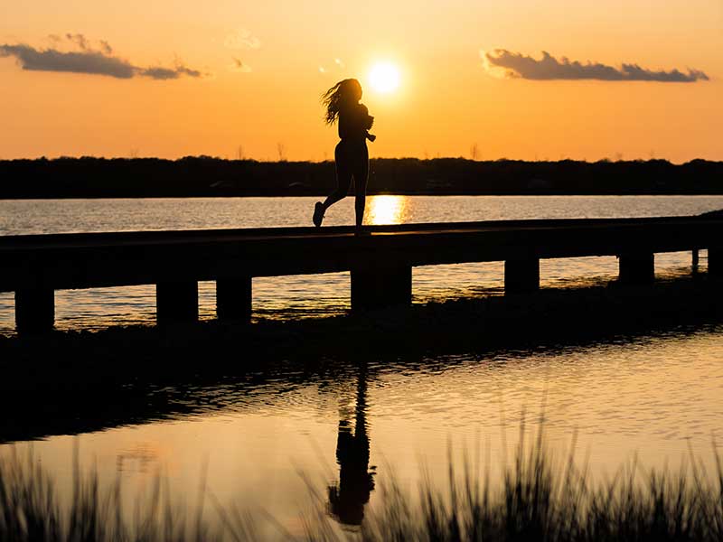 person running over a bridge, silhouetted by the sun