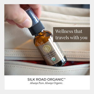 Bottle of essential oil with a dropper being used, labeled 'Silk Road Organic'.