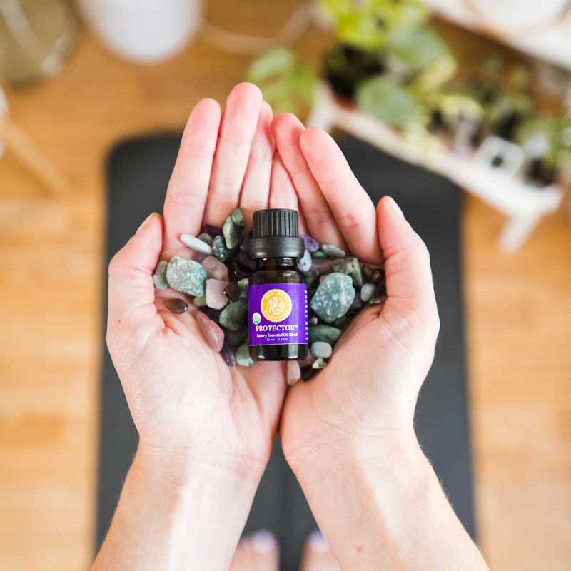 essential oils to boost immunity person holding protector essential oil blend bottle and gemstones