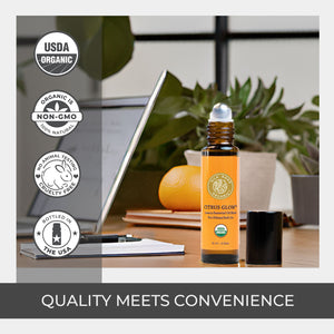 Roll-on bottle of 'Citrus Glow' on a desk with laptop and orange, USDA Organic and Non-GMO labels displayed. stainless steel rollerball amber glass bottle organic fractionated coconut carrier oil