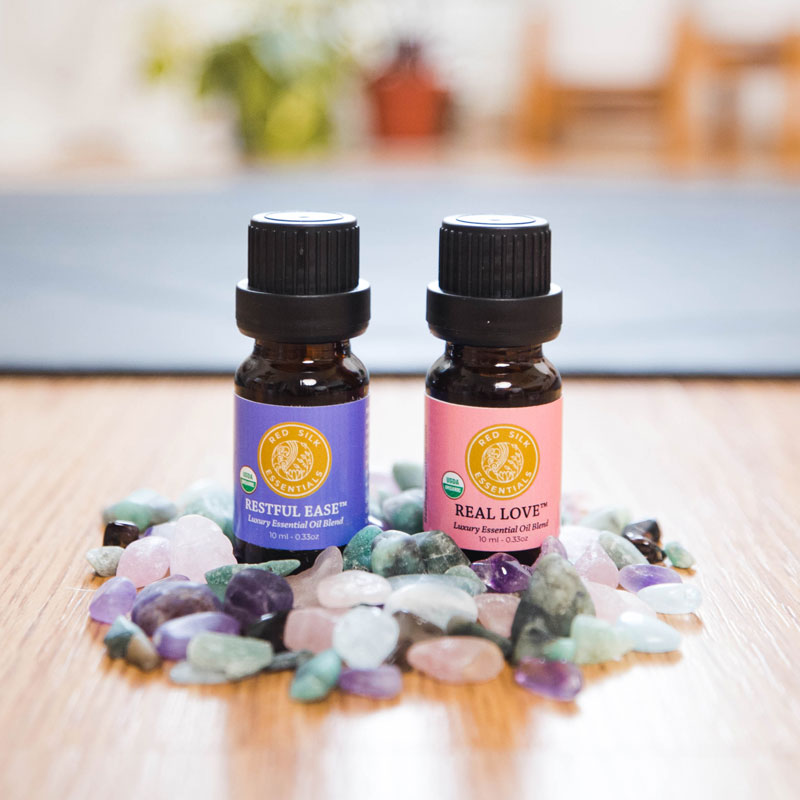 calming essential oils red silk essentials organic essential oil blend bottles restful ease and real love pictured with gemstones