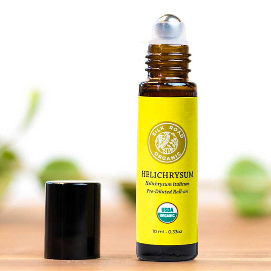 Roll-on bottle of Helichrysum oil with a yellow label on a wooden surface.