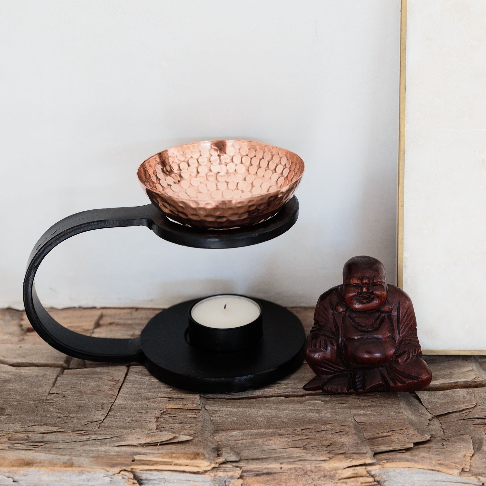 copper diffuser sitting on a shelf next to a carved wooden buddha